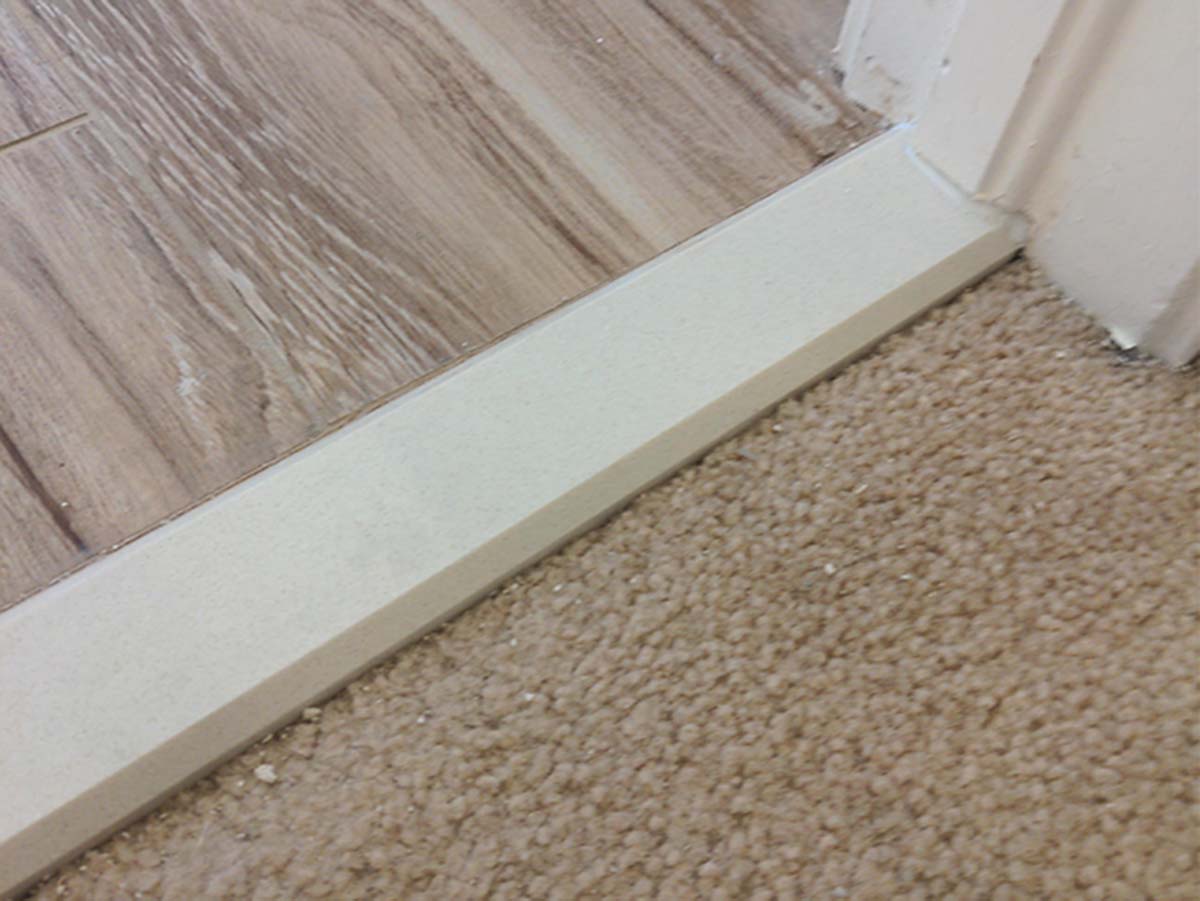 A solid surface threshold sits in between tile flooring and carpet